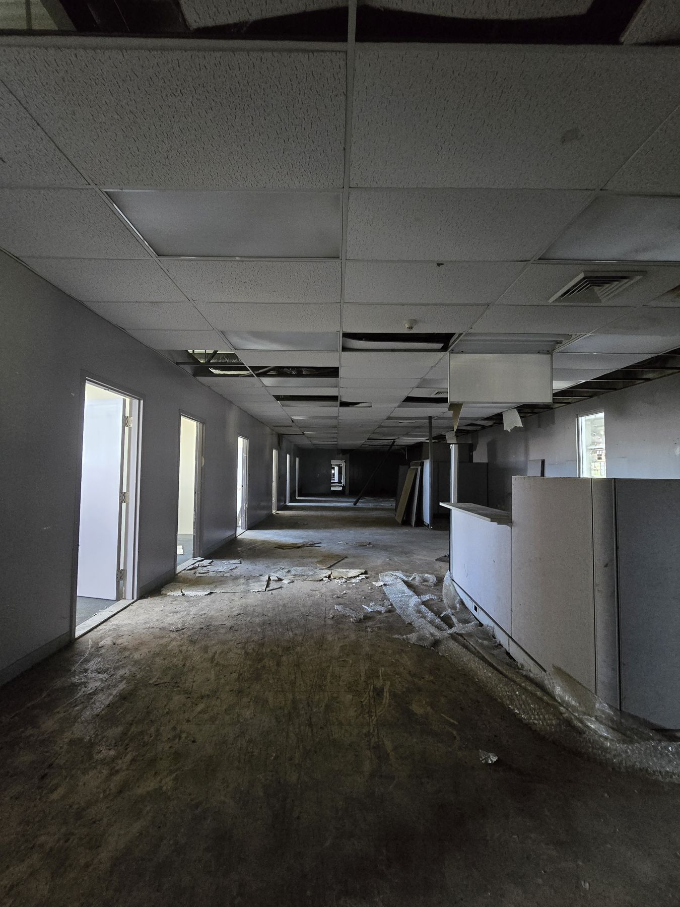 Pasillo de oficinas abandonadas con plafones caídos y cubículos vacíos