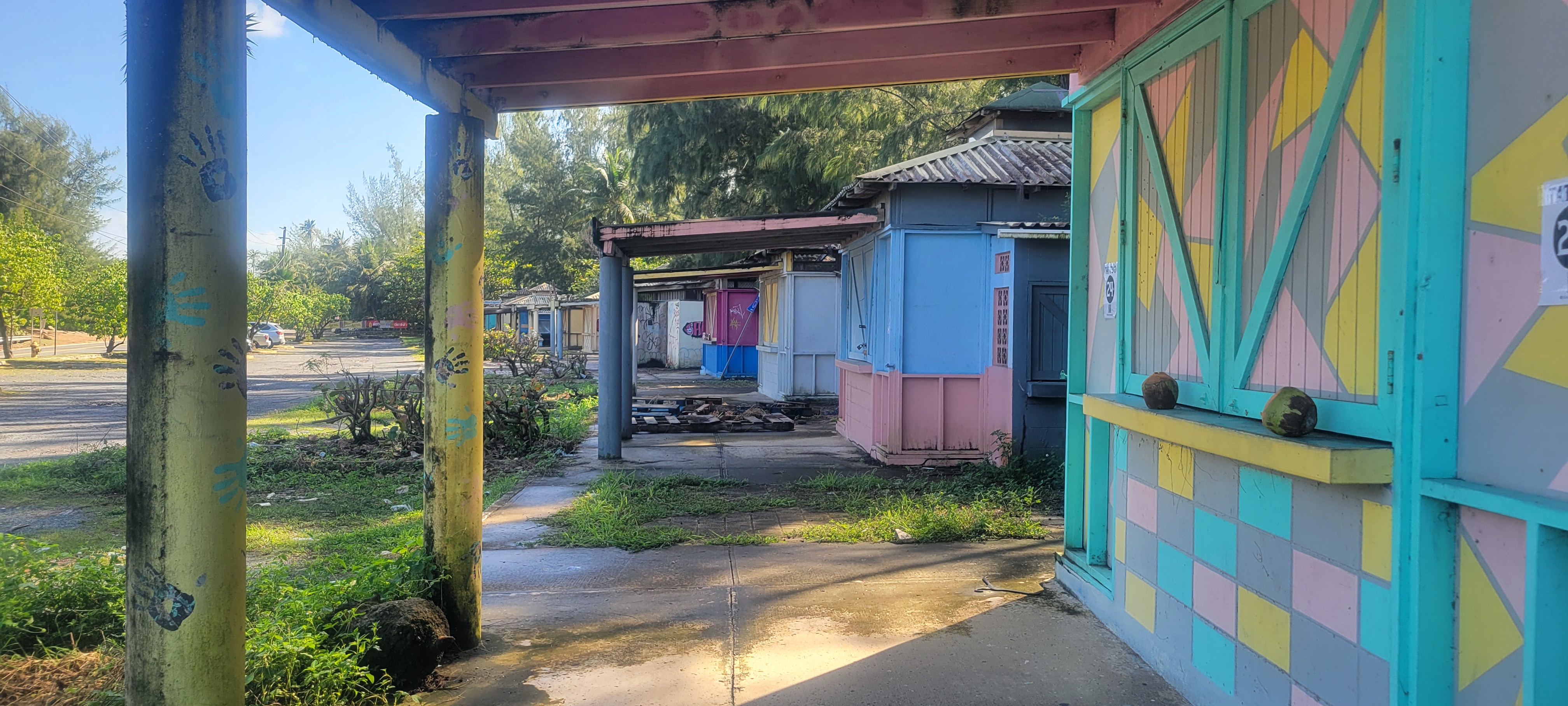 Quioscos abandonados en Loíza Puerto Rico con colores rosa azul y verde cerrados y con maleza creciendo entre las estructuras